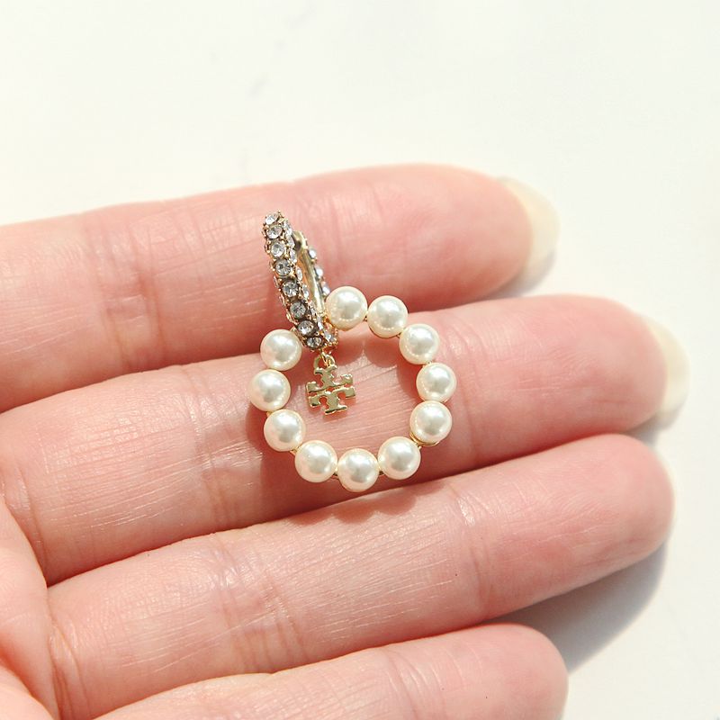 Close-up macro view of authentic tory burch moondance white pearl hoop earrings held in a person's palm showing scale.