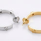 Macro shot of the Tory Burch logo engraving and high-shine silver finish on C-shaped hoops