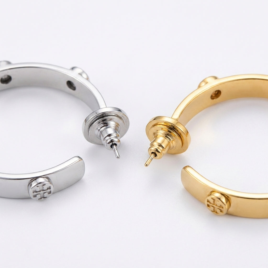 Macro shot of the Tory Burch logo engraving and high-shine silver finish on C-shaped hoops