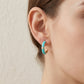 Close-up view of a model wearing turquoise blue enamel gold open hoop earrings.