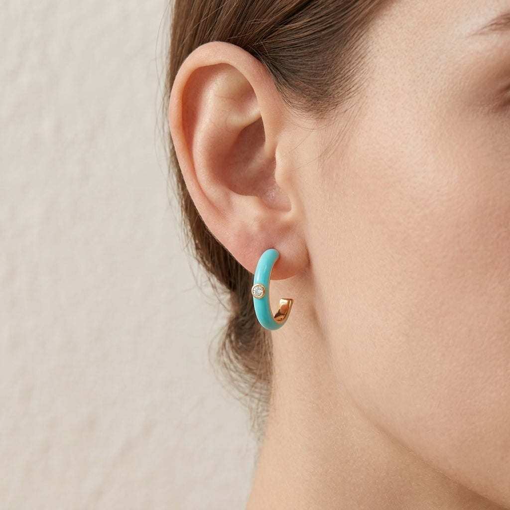 Close-up view of a model wearing turquoise blue enamel gold open hoop earrings.