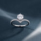 Round diamond six-prong v-shape chevron ring on dark textured backdrop.