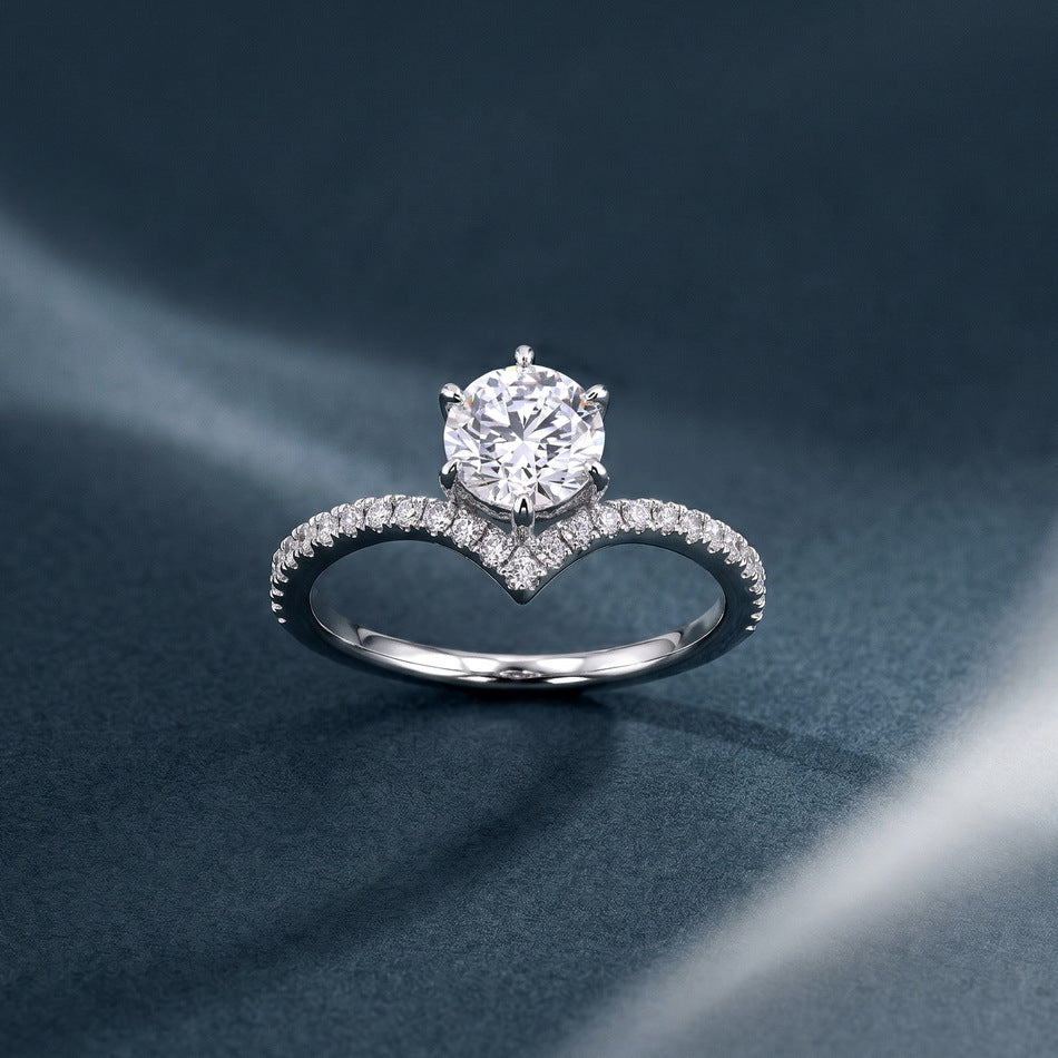 Round diamond six-prong v-shape chevron ring on dark textured backdrop.