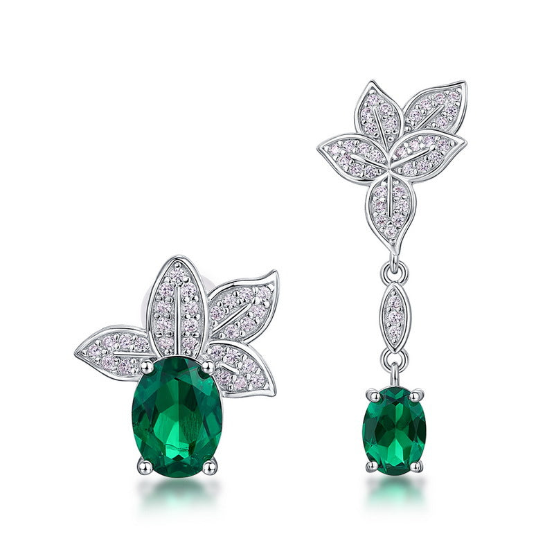 White background front view of a pair of vintage oval emerald asymmetric foliage dangle and stud earrings.