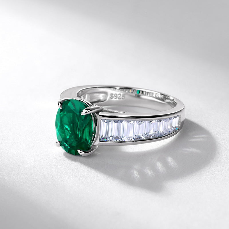 Silver ring with a green gemstone and diamond-studded band on a light gray background