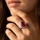 Close-up editorial portrait of a model holding her chin, displaying a vintage oval ruby criss-cross engagement ring.