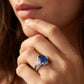 Close-up editorial portrait of a model holding her chin, displaying a vintage oval sapphire criss-cross engagement ring.