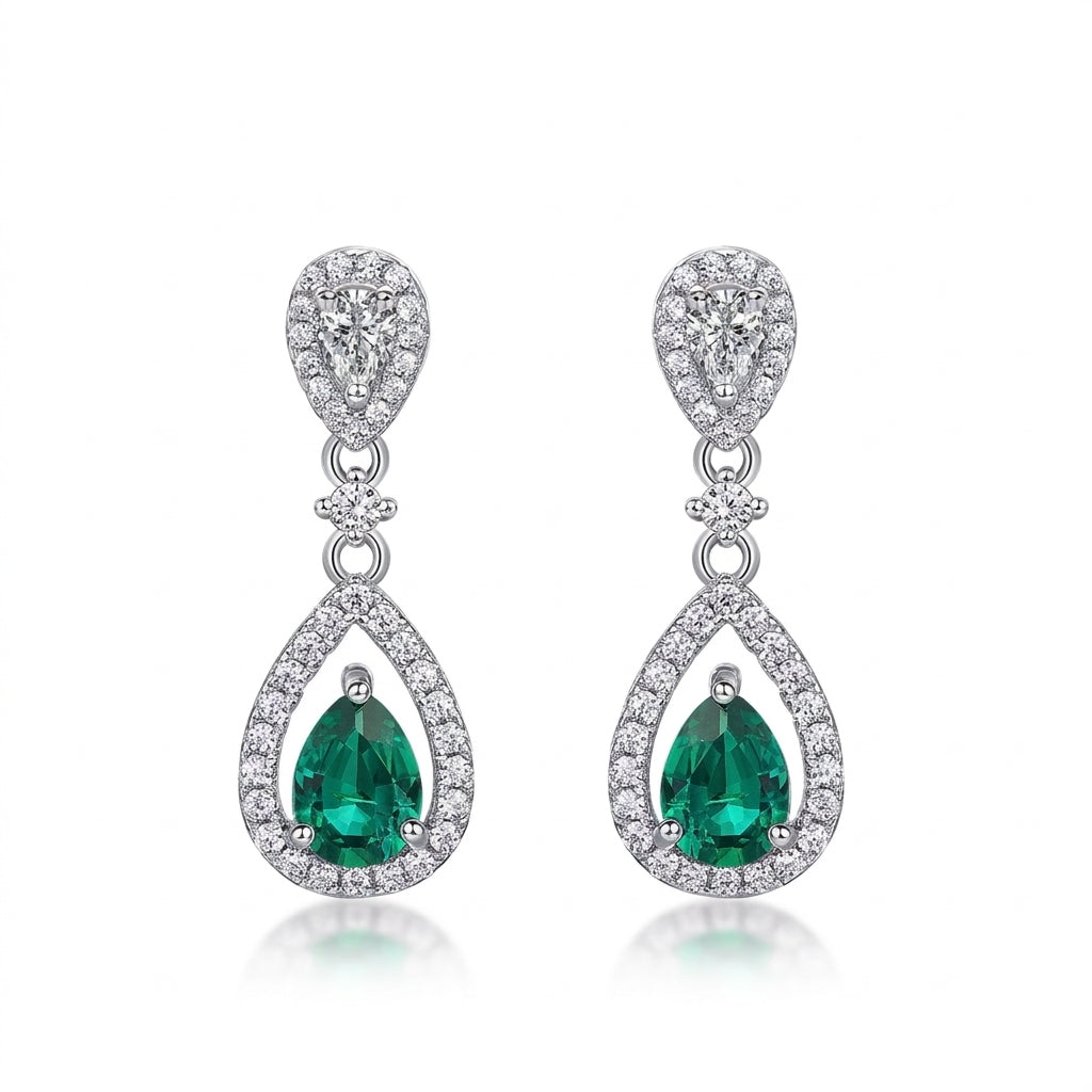 White background front view of a pair of vintage pear-cut emerald hollow halo drop earrings.