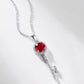 Side angle studio view of a vintage round-cut ruby key pendant necklace resting on a white shaded surface.