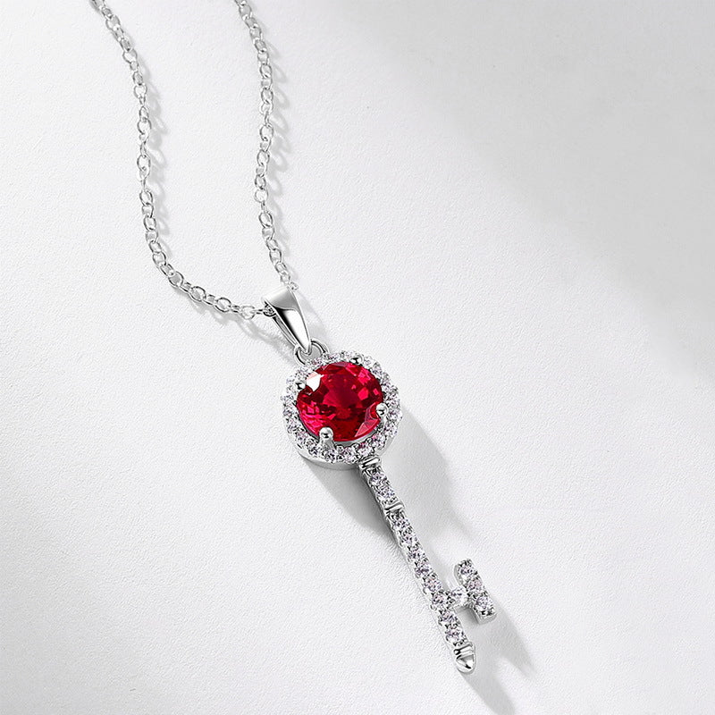 Side angle studio view of a vintage round-cut ruby key pendant necklace resting on a white shaded surface.