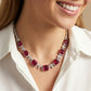 Close-up view of a smiling model wearing a vintage square ruby gala statement necklace over an elegant white silk blouse.