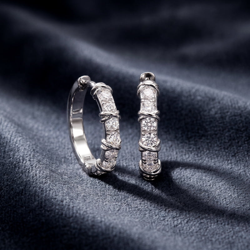 Angled shot of 1.2ctw x-cross ribbon diamond huggie earrings on dark silk.